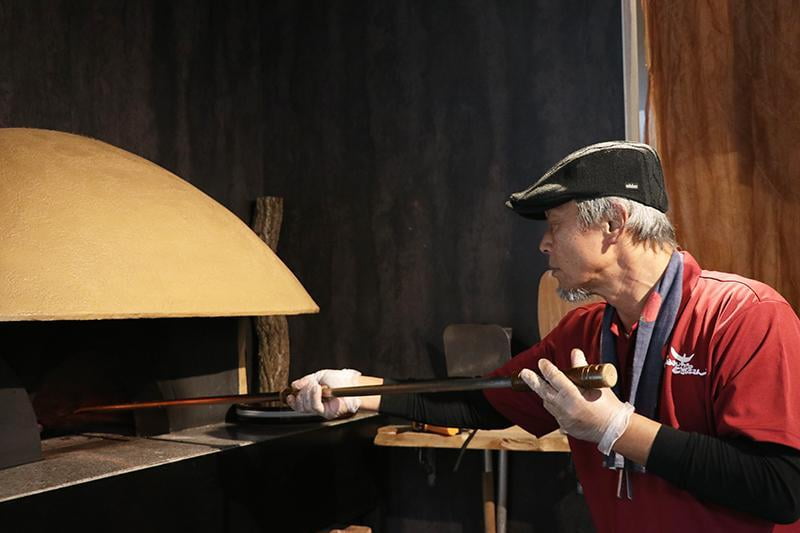 「さとうさんちのピザ屋さん」のピザ窯で、オーナーの佐藤さんが石窯焼きピザを焼く様子。