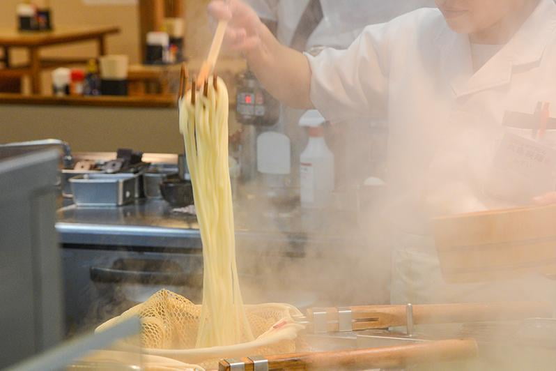 丸亀製麺の自家製麵のうどんをゆで汁から引き揚げている写真