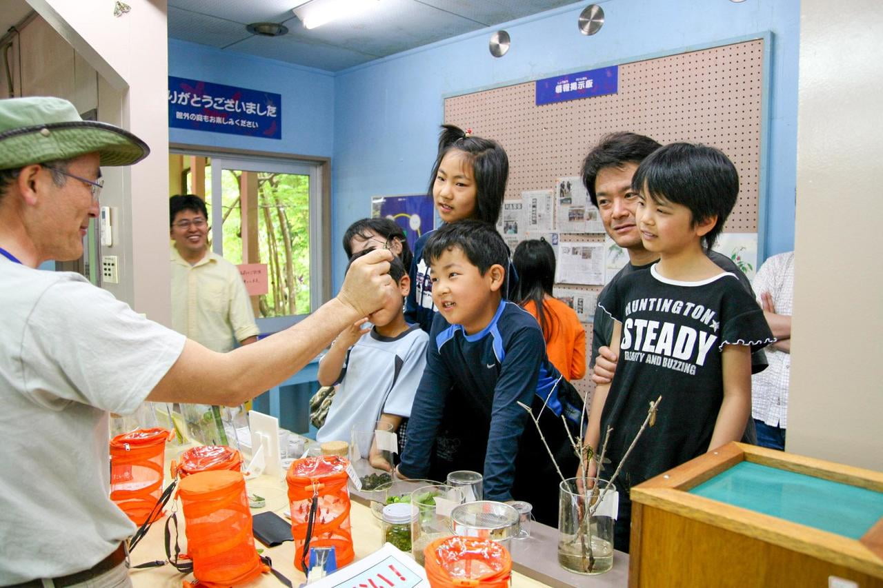 佐用町昆虫館ラボ内で虫をさわるスタッフと親子の写真