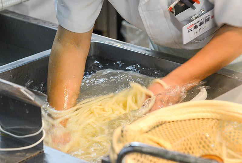 茹で上がった麺を水洗いしている写真