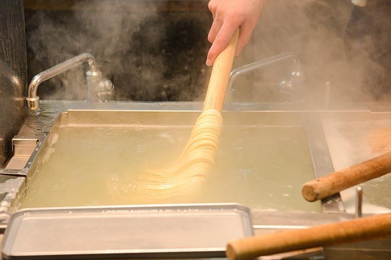 麺棒を使いうどんを茹でている写真