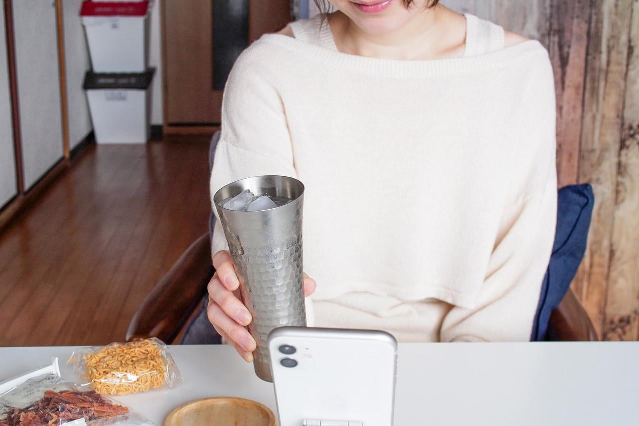 スマホでオンライン飲み会をする女性の写真